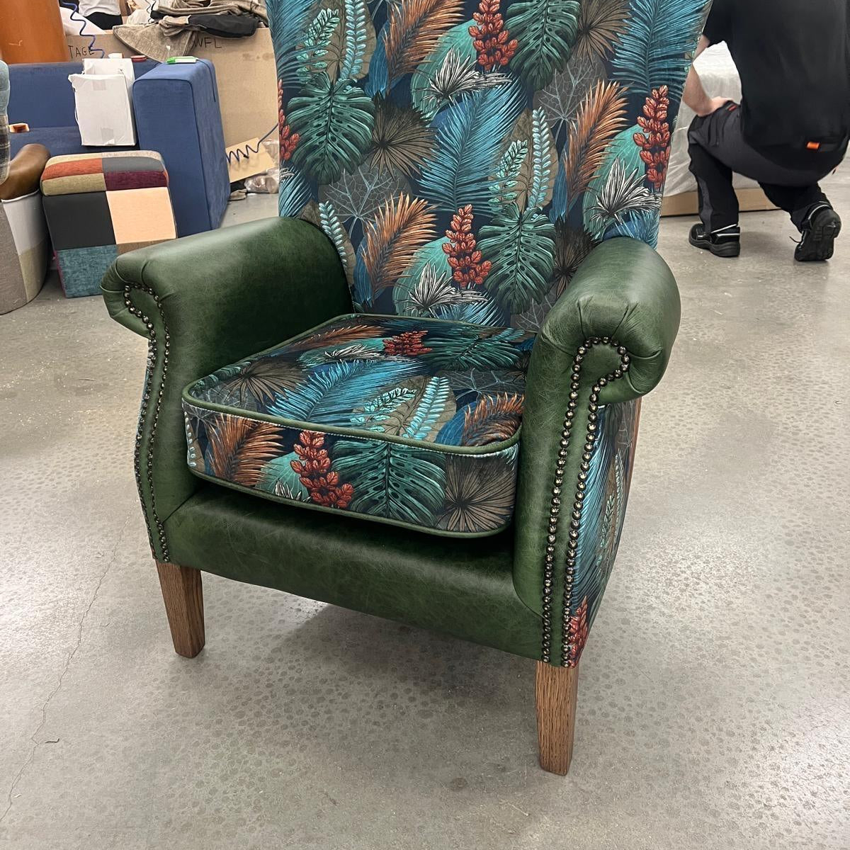 Green armchair with tropical leaf patterned upholstery and wooden legs in showroom