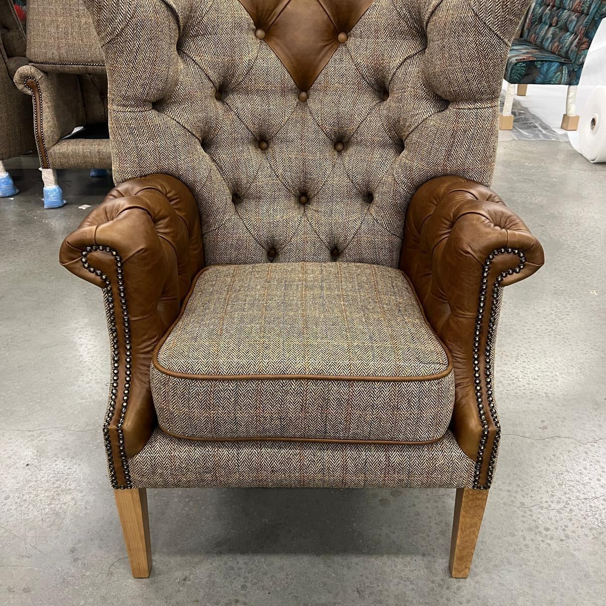 Button-tufted high back armchair with brown leather arms and herringbone fabric upholstery