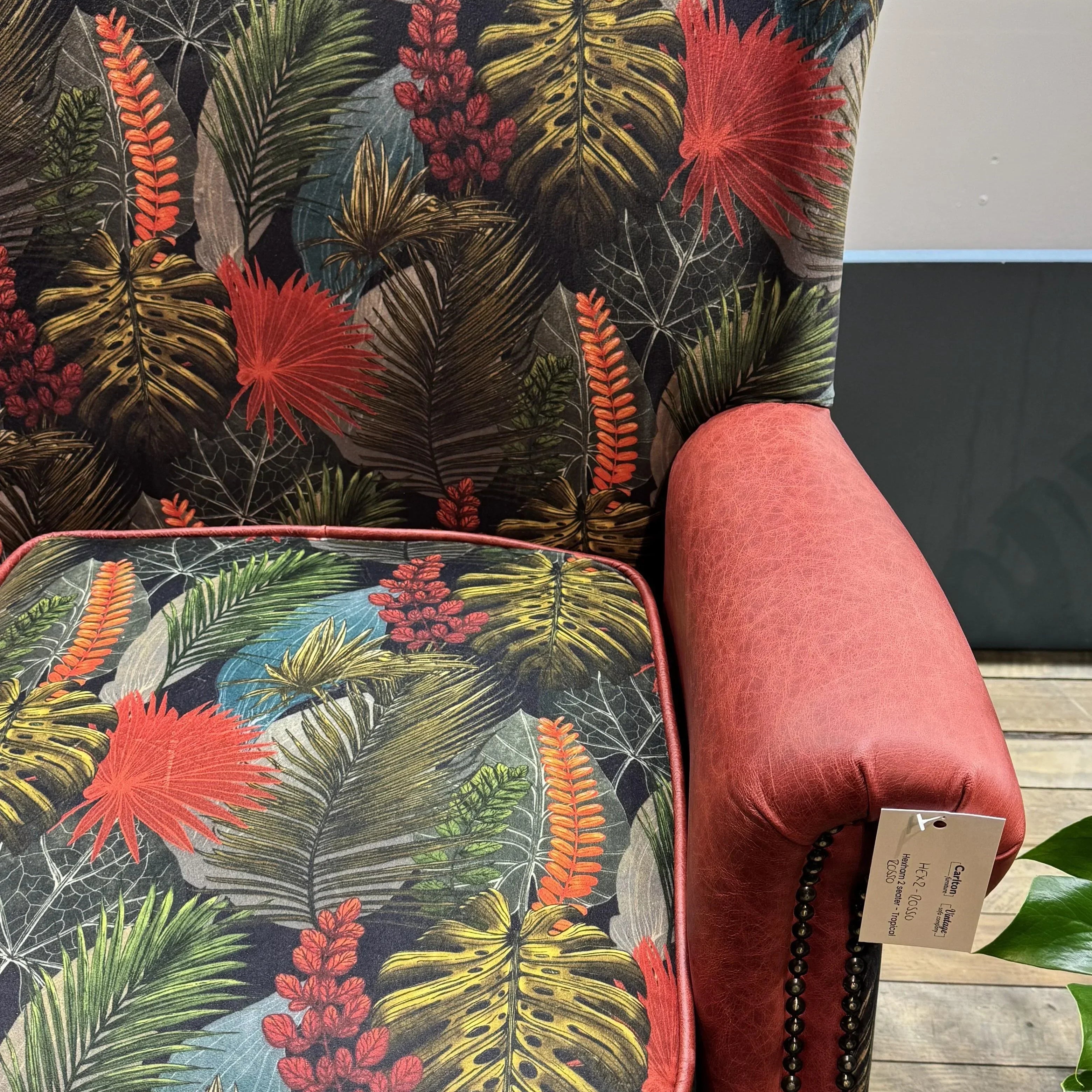 Accent armchair with tropical leaf upholstery and red faux leather armrest on wooden floor