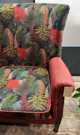 Accent armchair with tropical leaf upholstery and red faux leather armrest on wooden floor