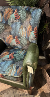 Patterned armchair with tropical leaf upholstery and green leather armrest on wooden floor