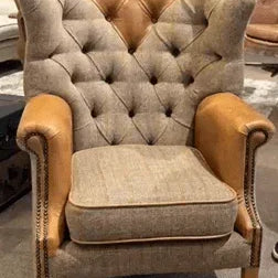Tufted fabric armchair with tan leather arms and wooden legs in showroom setting