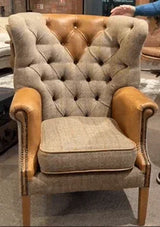 Tufted fabric armchair with tan leather arms and wooden legs in showroom setting