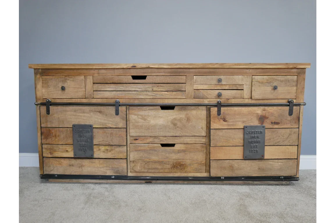 Rustic wooden sideboard with sliding metal doors and multiple drawers on carpeted floor