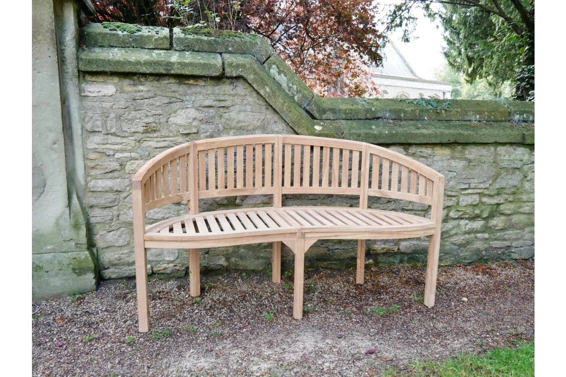 Curved wooden garden bench with slatted seat and backrest placed against stone wall