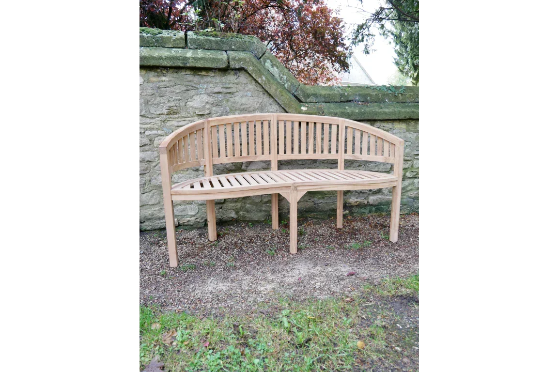 Curved wooden garden bench with slatted seat and backrest against stone wall outdoors