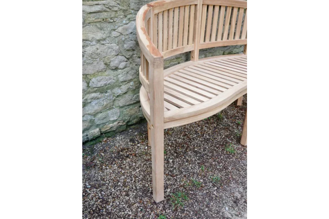 Curved wooden garden bench with slatted seat and backrest against stone wall