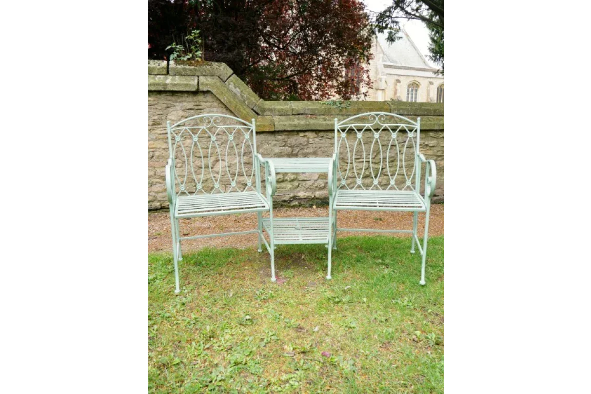 Metal garden bench seat with ornate design and small central table on lawn