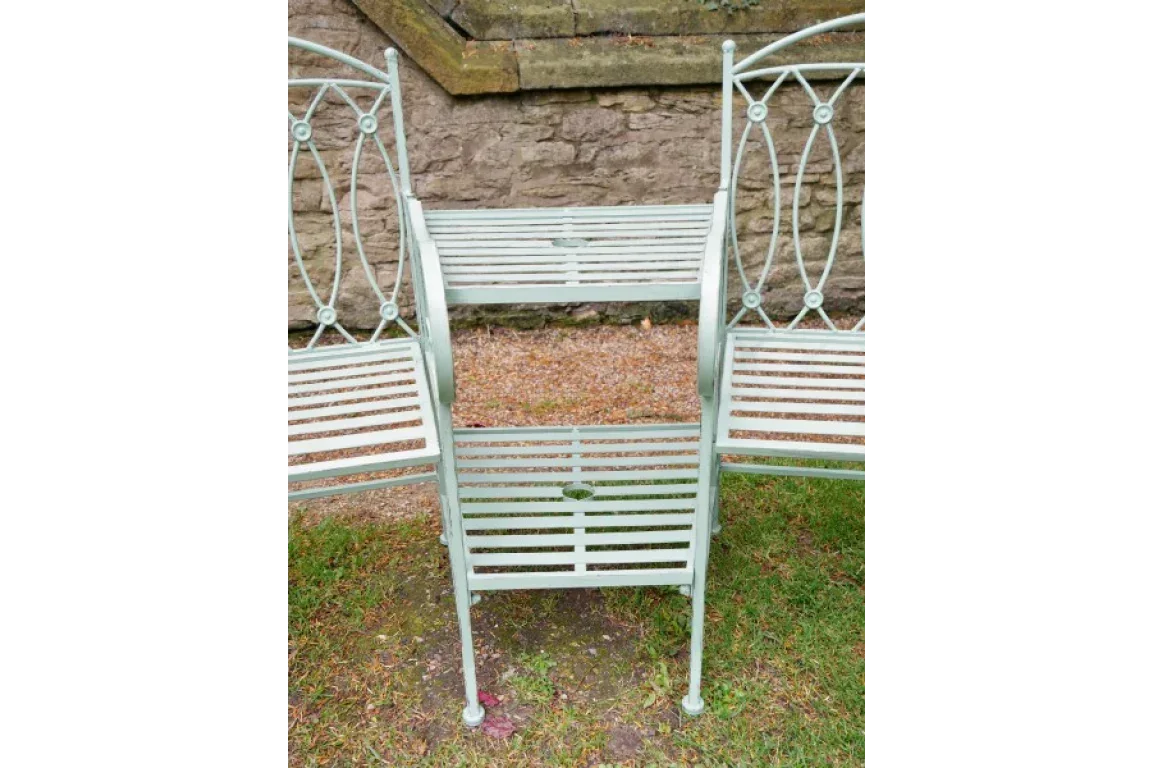 Metal garden bench with pale green slatted seats and intricate backrest design on grass