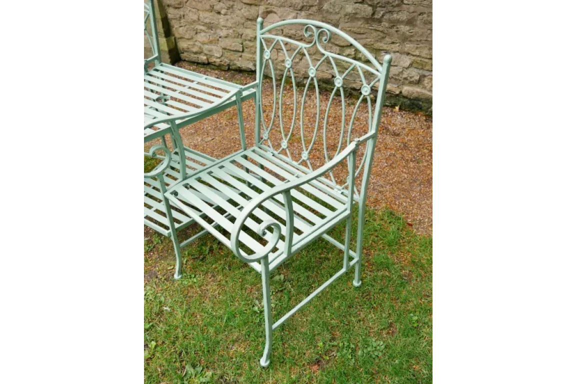 Light green metal garden chair with ornate backrest and slatted seat on grass