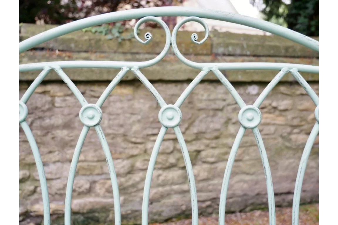 Close view of metal garden bench backrest with scrollwork detail against stone wall