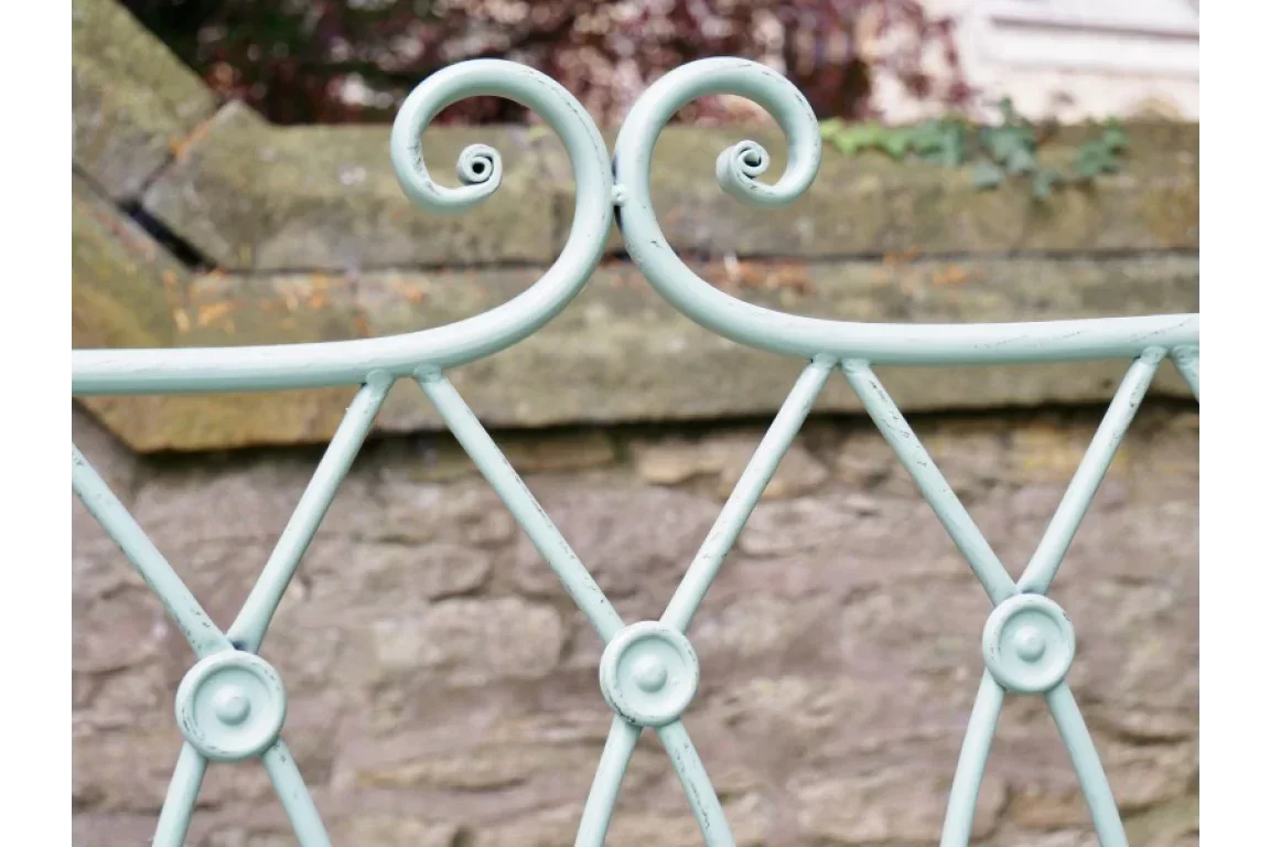 Close up of vintage metal headboard with swirl detail and distressed pale green finish