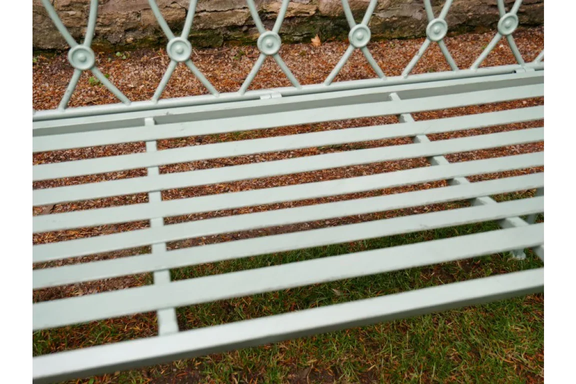 Metal garden bench with slatted seat and decorative backrest on grass and gravel