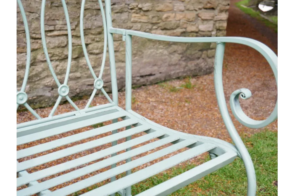 Light green metal garden bench with decorative scroll armrest on gravel and grass