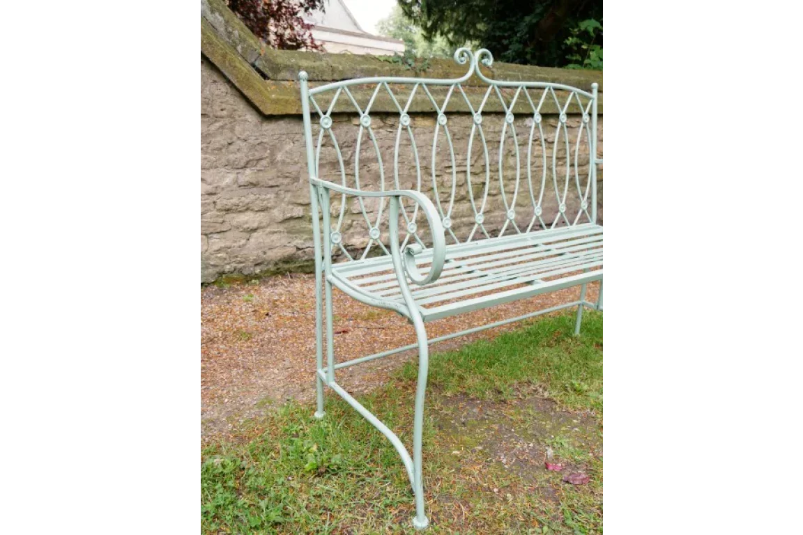 Light green metal garden bench with curved armrest and ornate backrest on grass