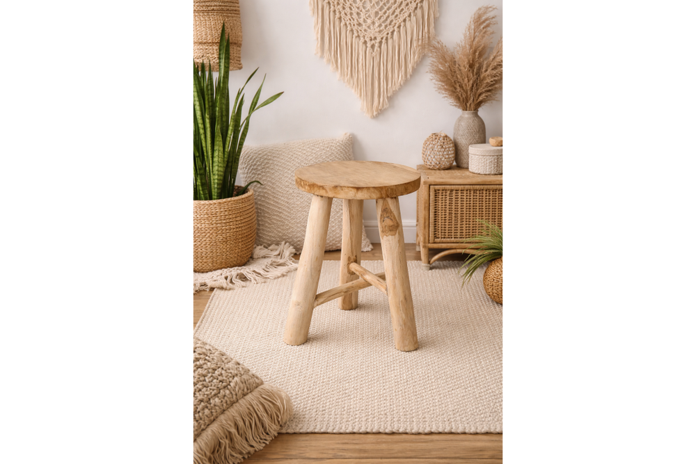Round wooden stool with three legs in a beige, bohemian-style room setting with plants and woven decor.