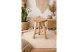 Round wooden stool with three legs in a beige, bohemian-style room setting with plants and woven decor.