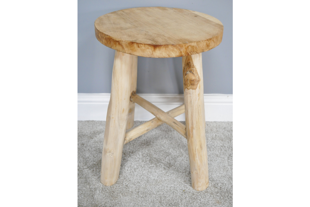 Round wooden stool with three legs and cross support, light natural wood finish, front angle on carpeted floor.