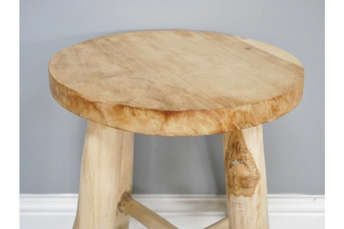 Round natural wood stool with three thick legs, front angled view against a gray wall background.