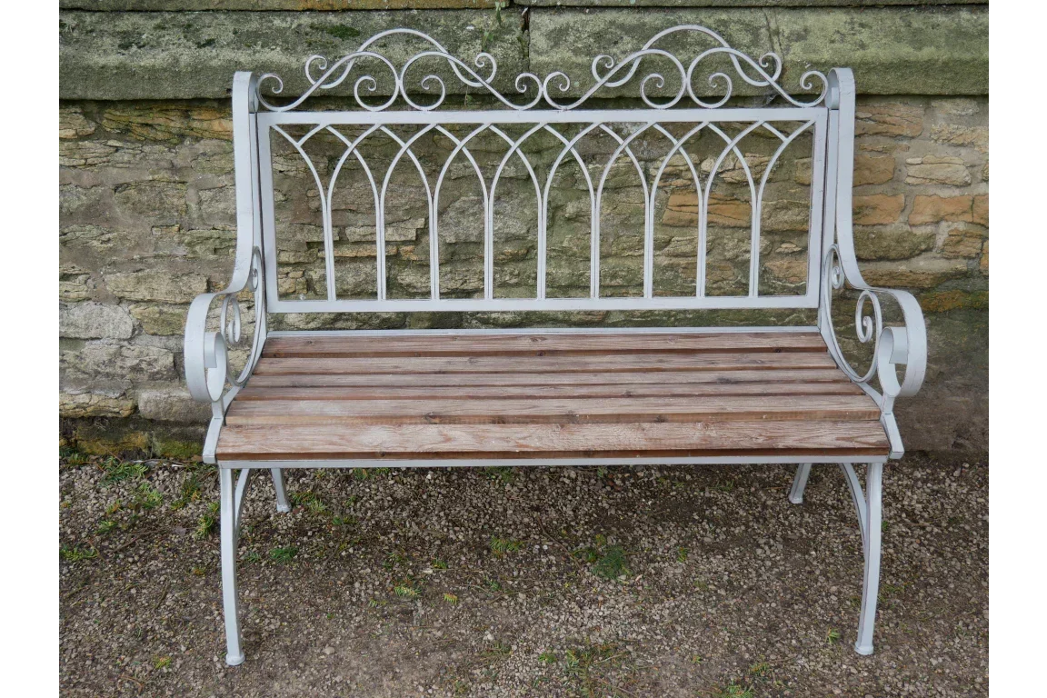 Metal garden bench with wooden slats and decorative backrest against stone wall