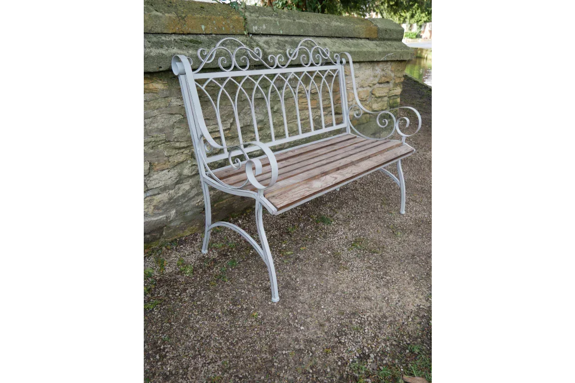 Ornate metal and wood garden bench with scroll arms placed beside a stone wall outdoors