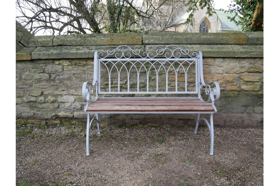 Metal garden bench with wooden seat slats and ornate backrest against stone wall