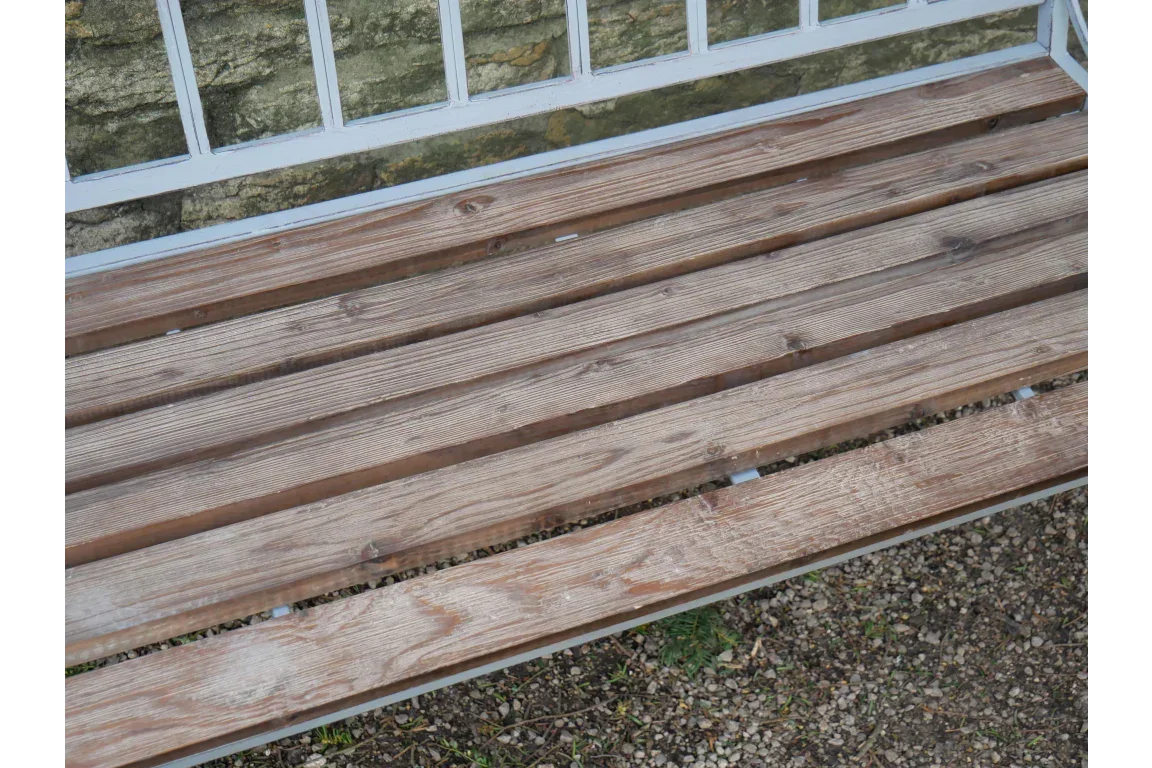 Wooden garden bench seat with horizontal slats and metal frame on gravel patio