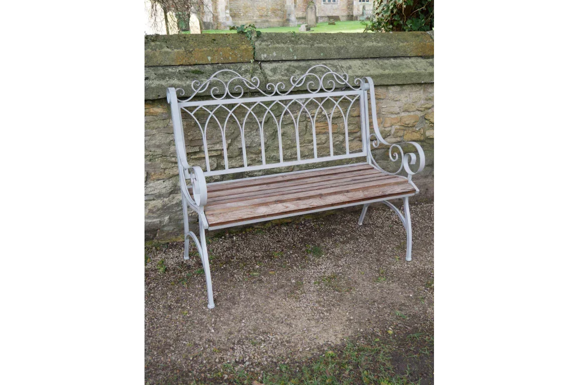 Metal and wood garden bench with ornate backrest set against a stone wall outdoors