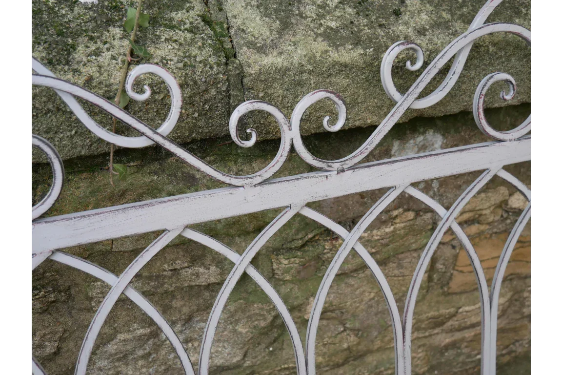 distressed white metal garden fence with scroll detail against stone wall