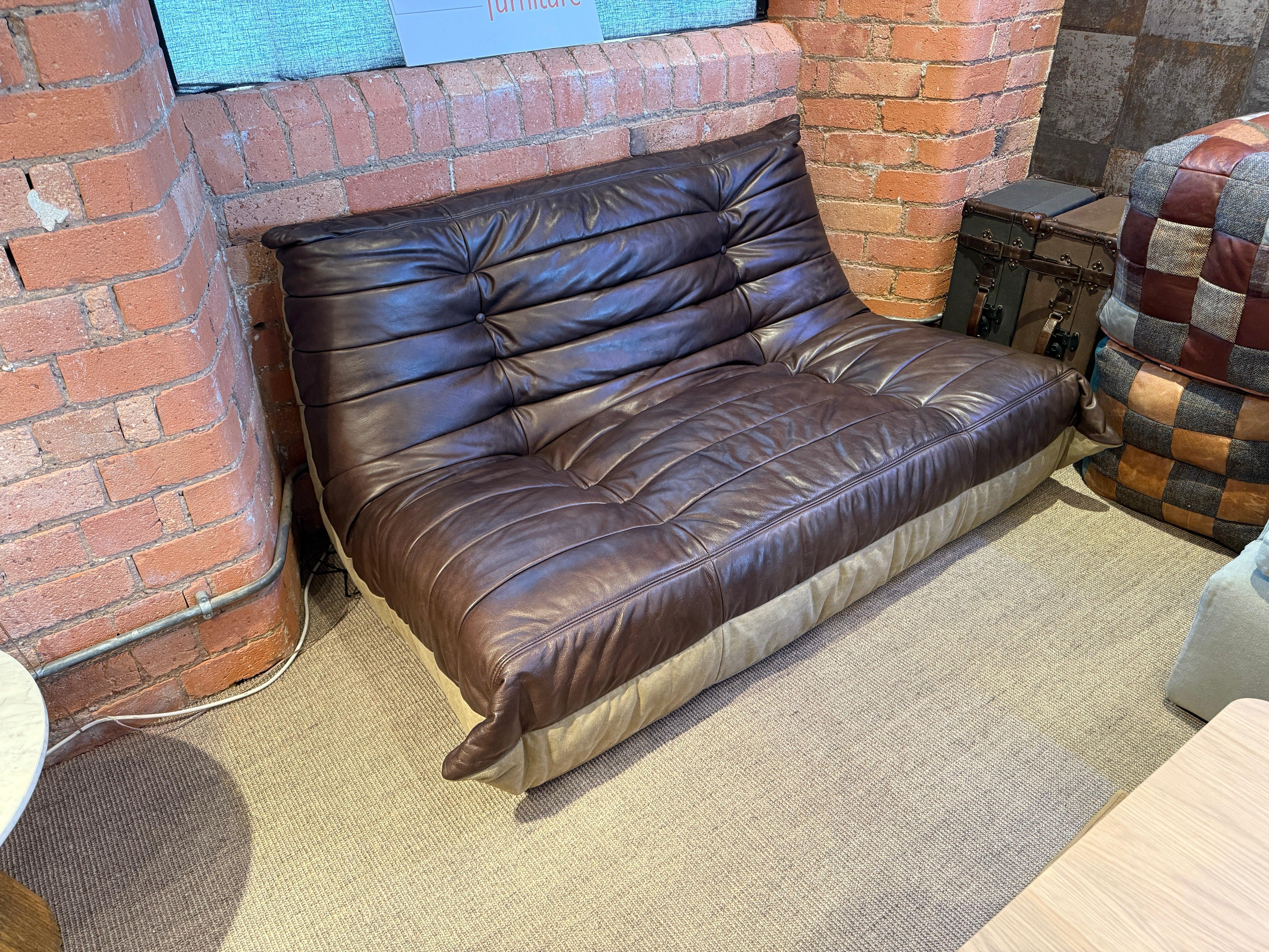 Brown leather sofa with tufted seat and backrest against exposed brick wall