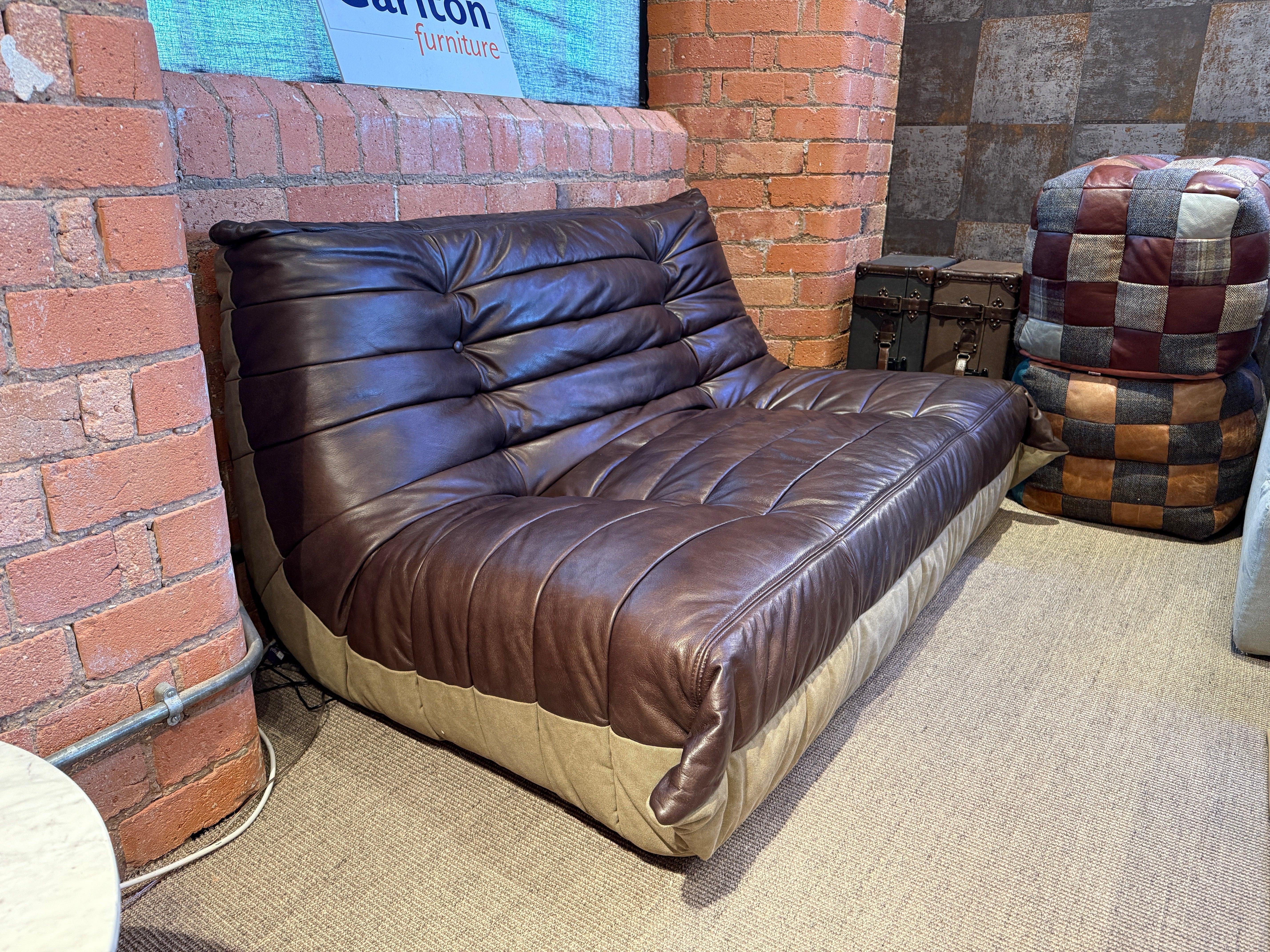 Brown leather sofa with tufted seat and back, set against exposed brick wall