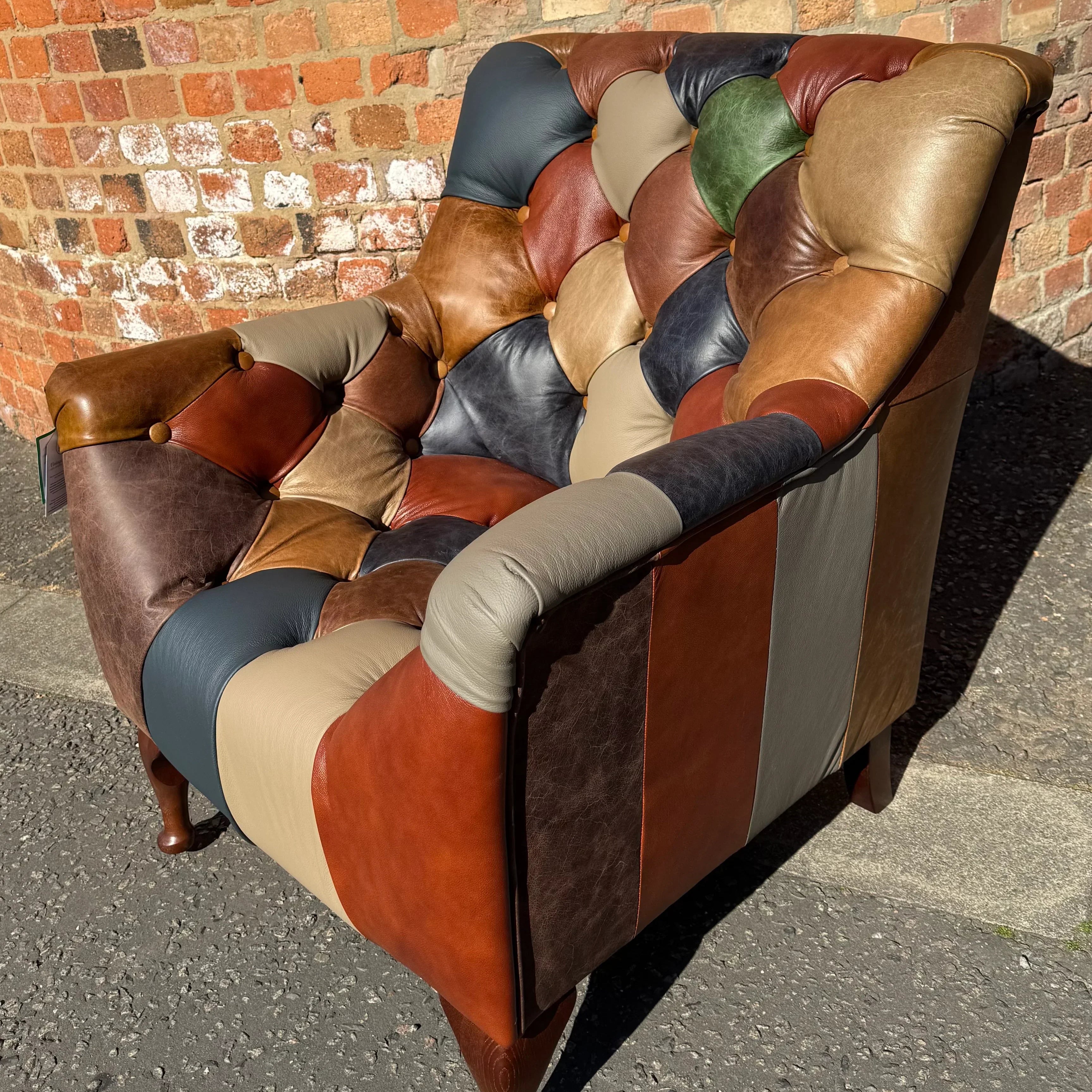 Patchwork leather armchair with button-tufted backrest against brick wall outdoors