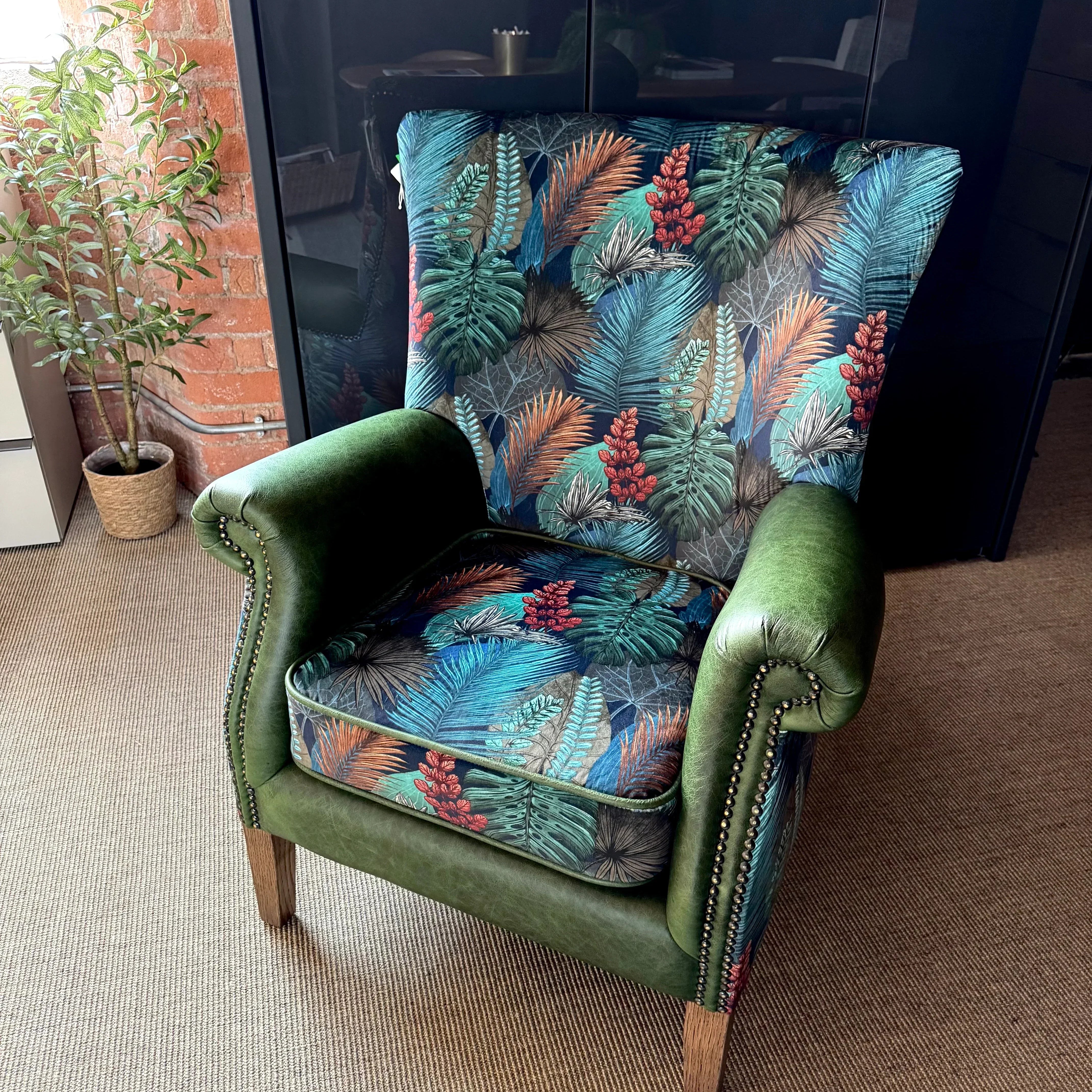 Green velvet armchair with tropical leaf patterned upholstery and wooden legs