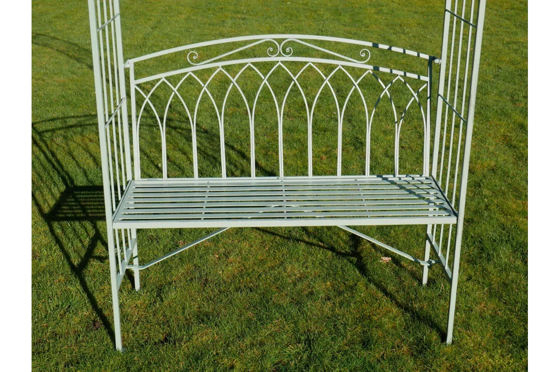 Pale green metal garden bench with decorative arched backrest on grass lawn