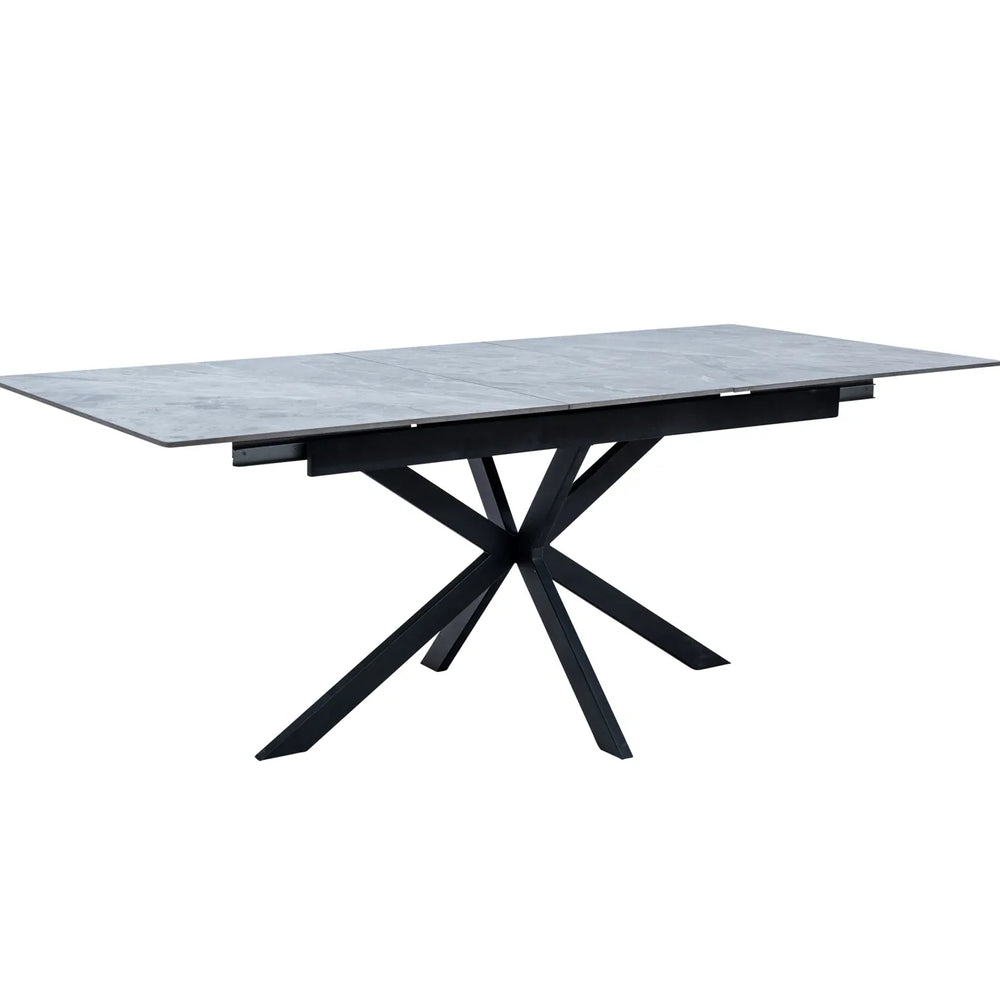 A rectangular dining table with a gray stone-look top and a black metal X-shaped pedestal base, shown on a plain white background.
