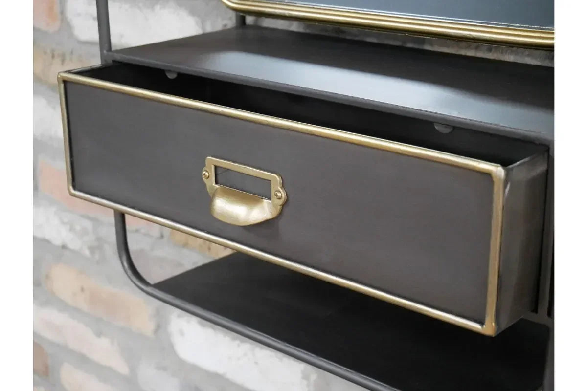 Black metal drawer unit with gold trim and handle against a brick wall