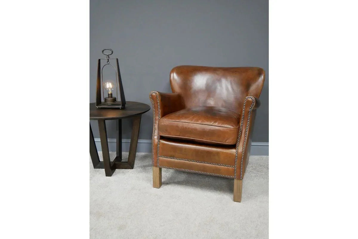 Brown leather armchair with studded trim beside dark wood side table and lamp