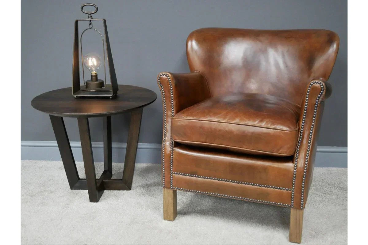 Brown leather armchair with studded trim next to dark wood side table and decorative lamp