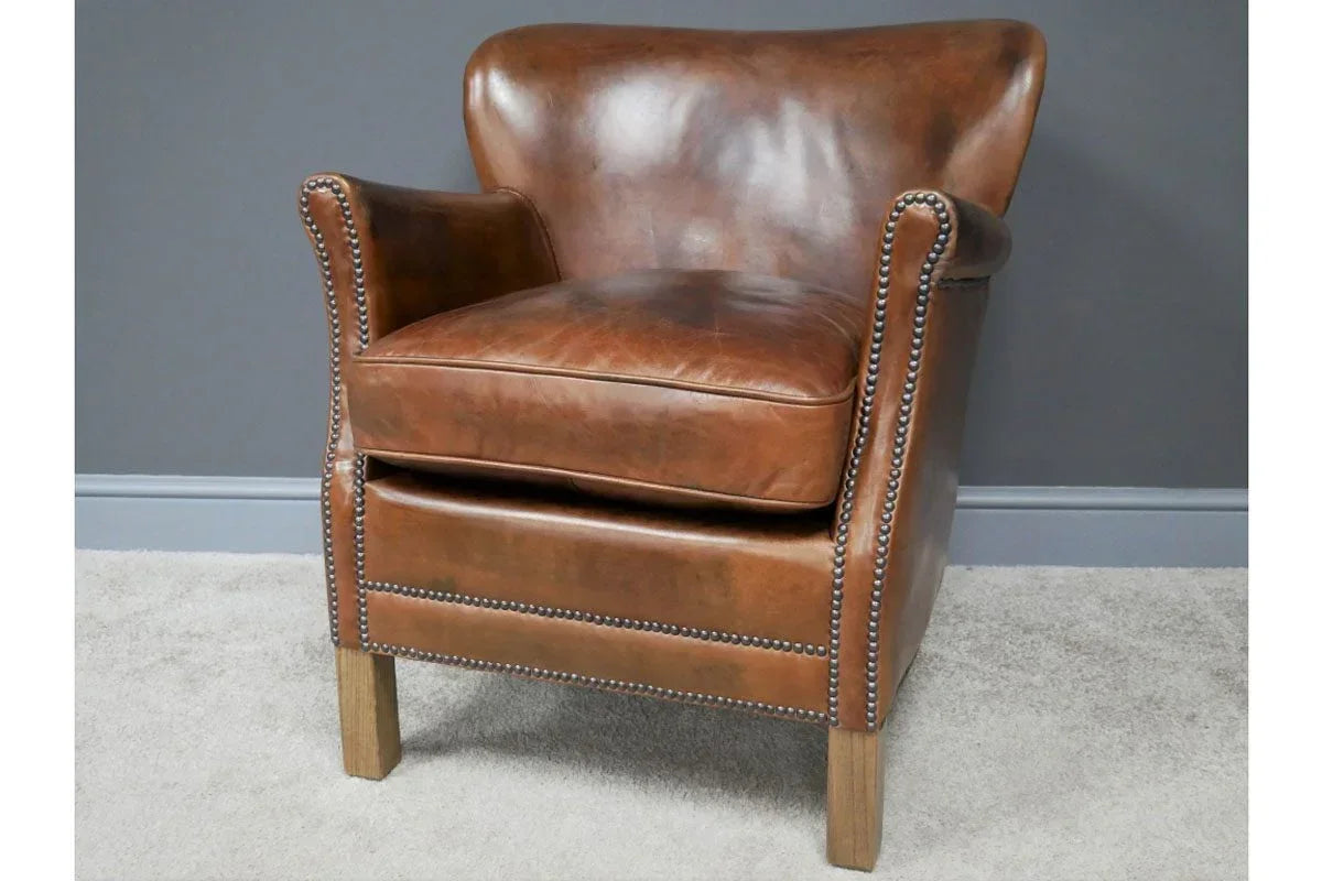 Brown leather armchair with studded trim and wooden legs on light carpet