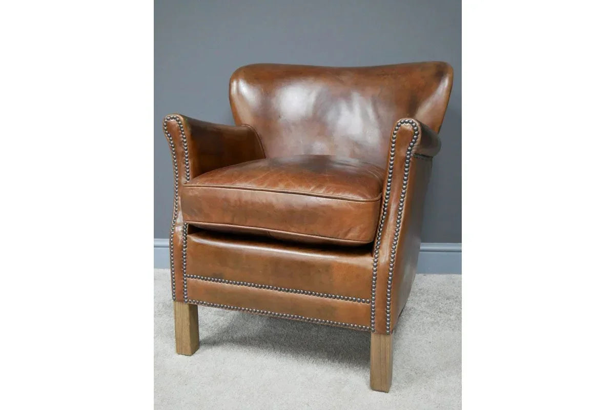 Brown leather armchair with nailhead trim and wooden legs on light carpet