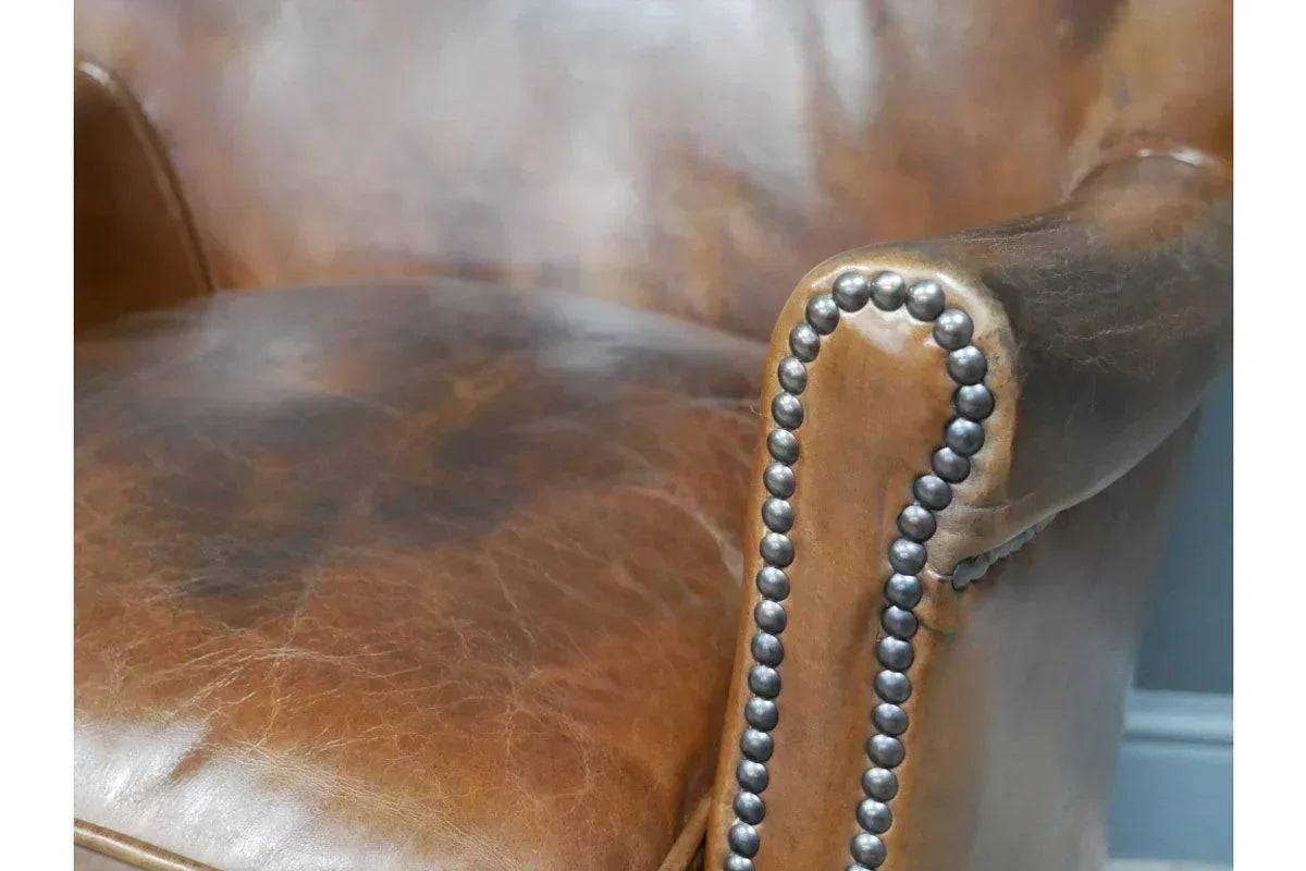 Closeup of brown leather armchair with studded armrest detailing