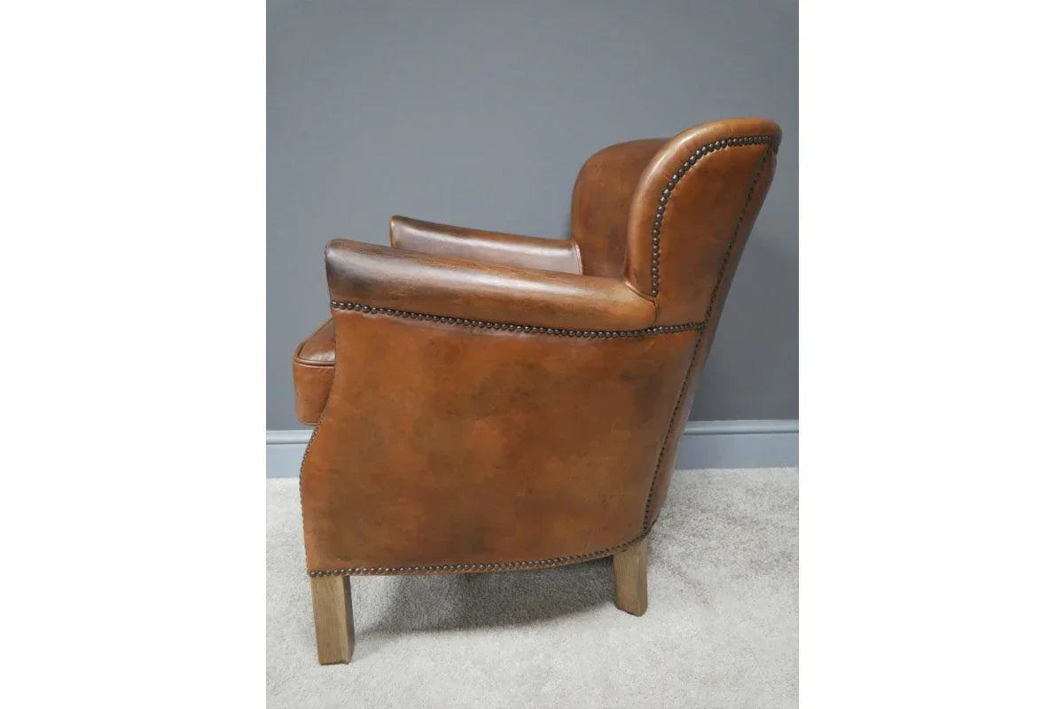 Side view brown leather armchair with studded trim and wooden legs on carpeted floor