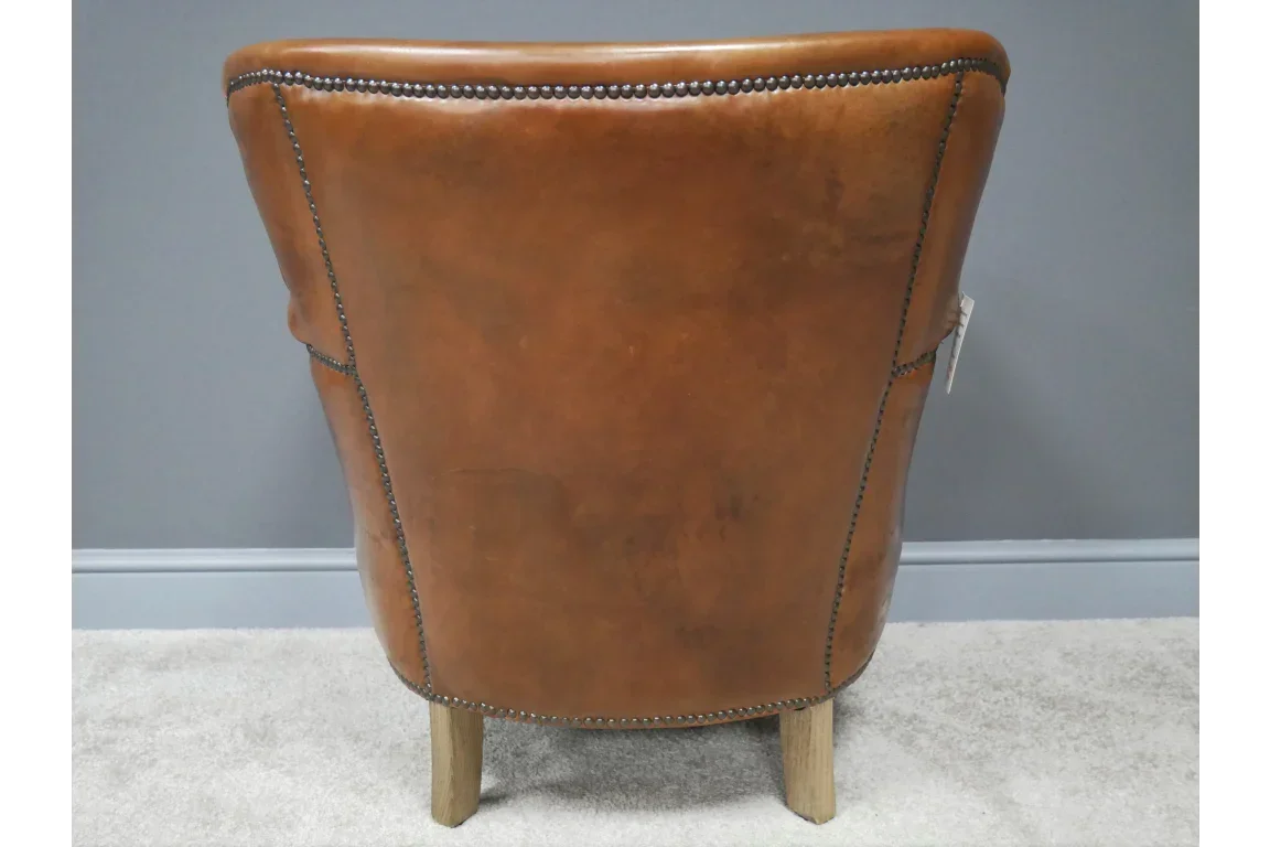 Brown leather accent chair with studded trim and wooden legs, rear view against grey wall