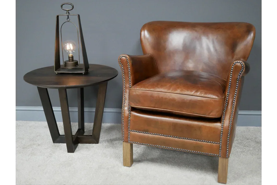 Brown leather armchair with stud detail beside dark wood side table and decorative lamp