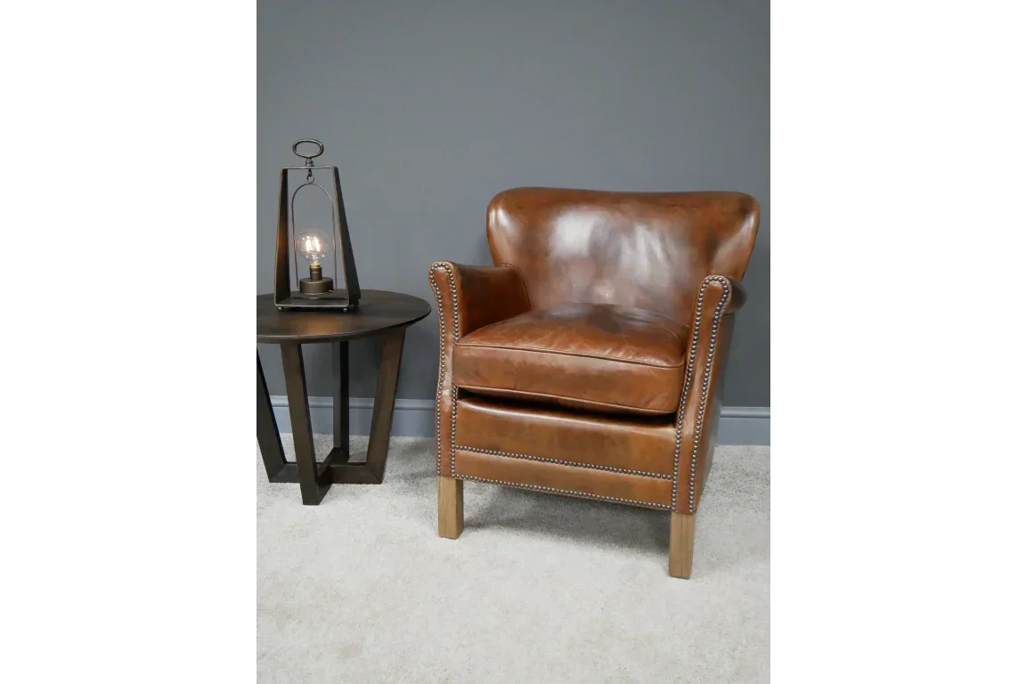 Brown leather armchair with wooden legs beside dark wood lamp table on light carpet