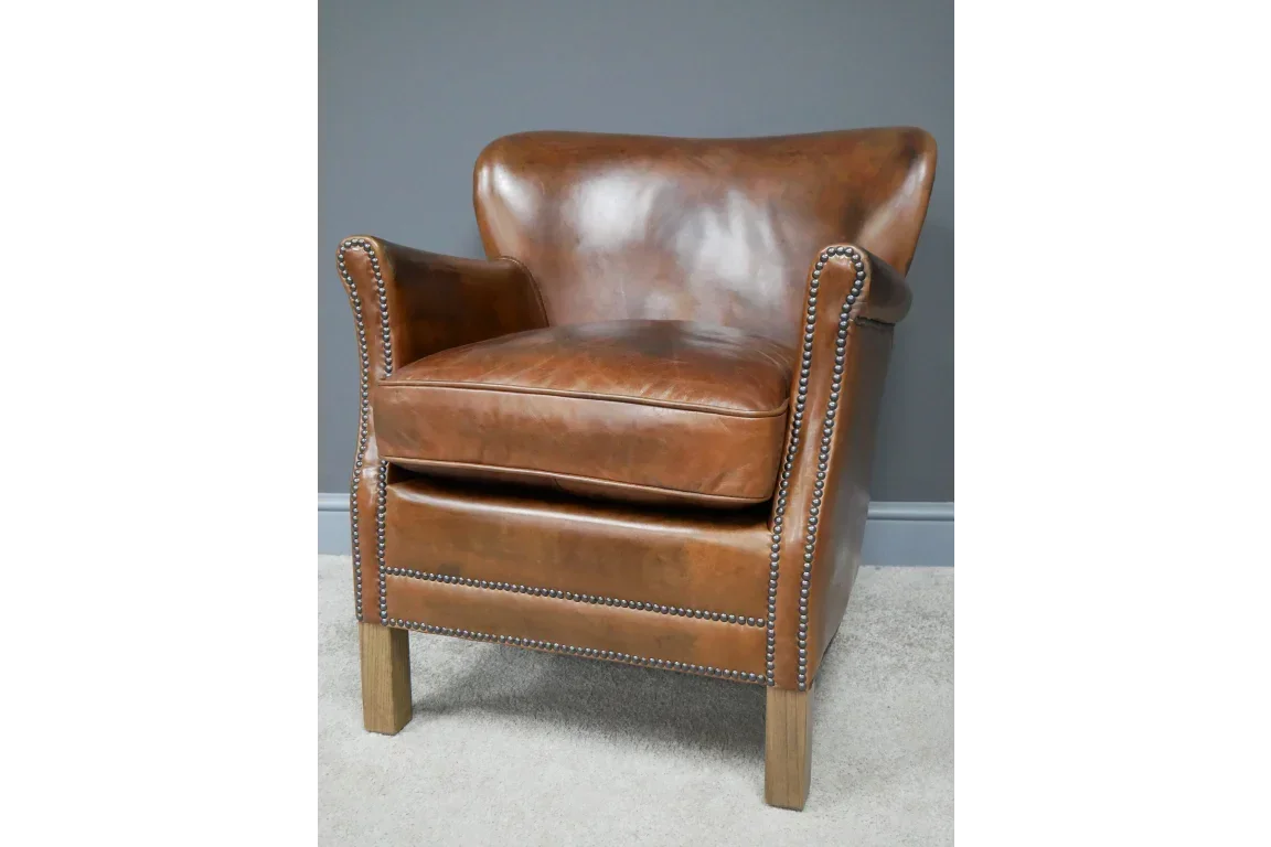 Brown leather armchair with studded trim and wooden legs against a grey wall