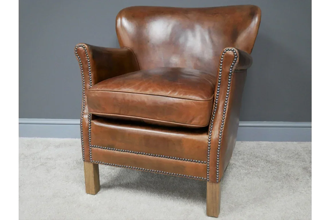 Brown leather armchair with studded trim and wooden legs against grey wall