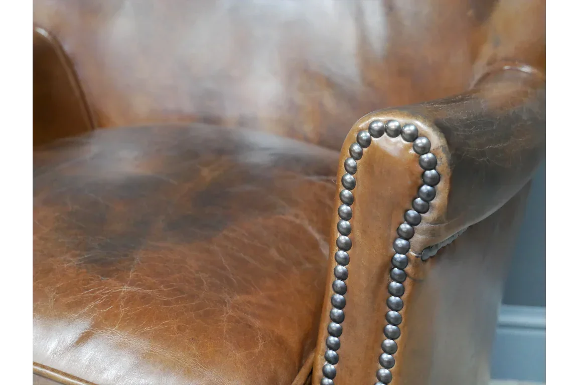Brown leather armchair with metal stud detailing on armrest close-up