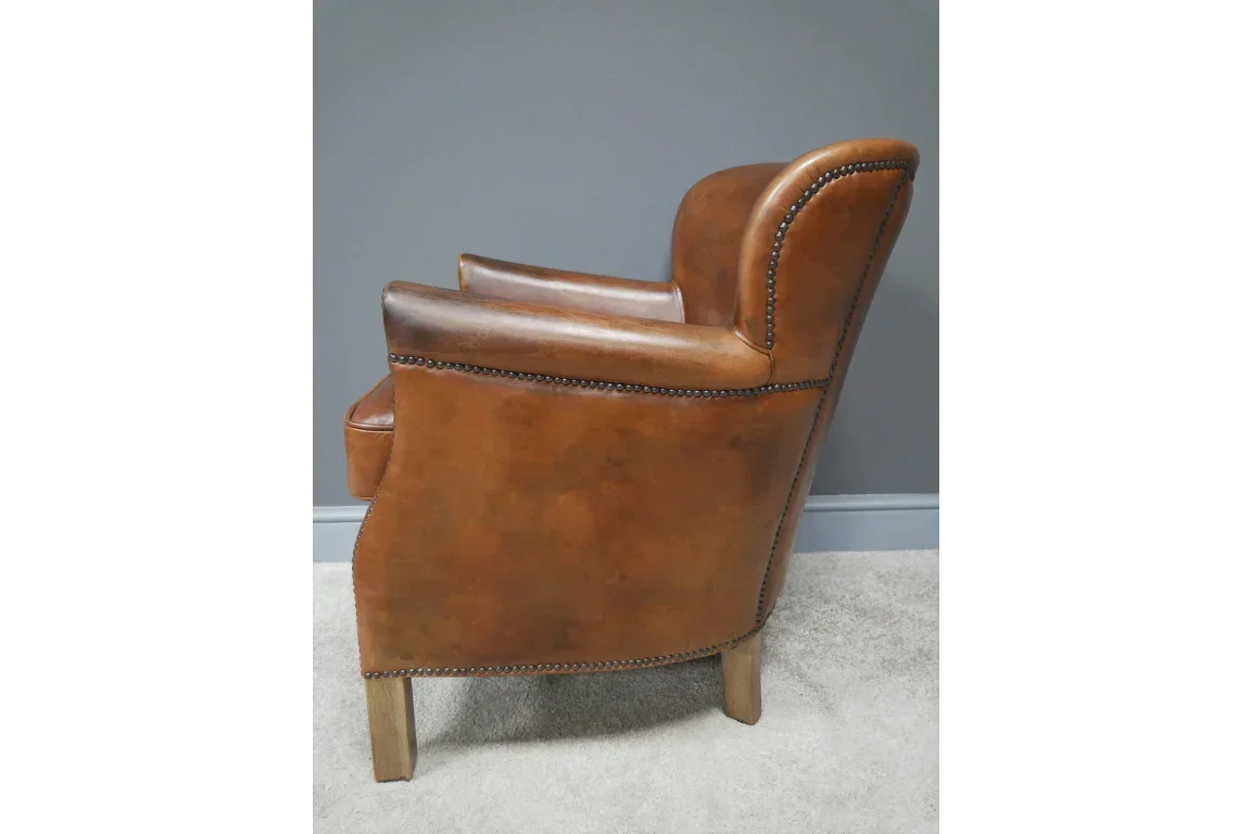 Brown leather armchair with nailhead trim and wooden legs, side profile view