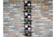 Black metal vertical wine bottle holder mounted on a multicolored brick wall, holding alternating bottles horizontally.